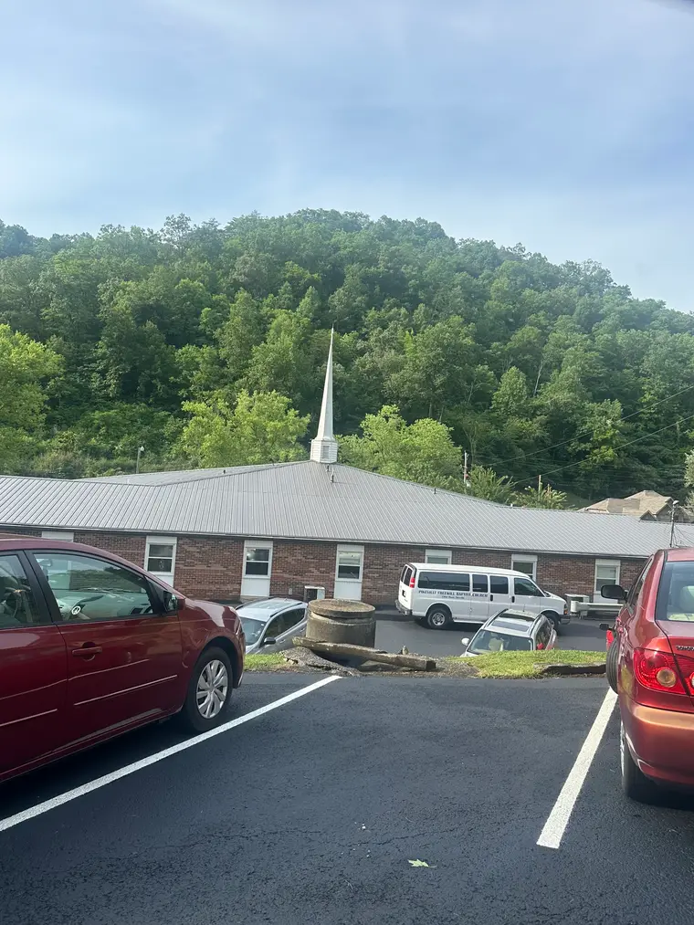 Brick church with a white steeple and a new charcoal standing-seam metal roof, wooded hillside rising behind it
