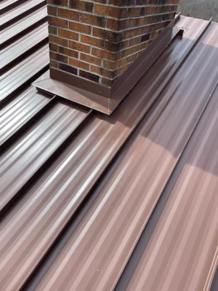 Brown standing-seam metal roof with custom brown sheet-metal flashing wrapped around a brick chimney