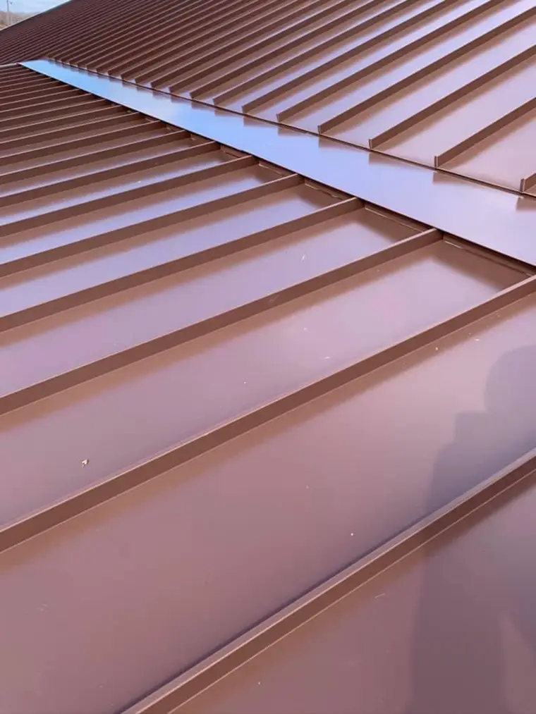 Close-up of copper-brown standing-seam metal roof panels meeting cleanly at a hip