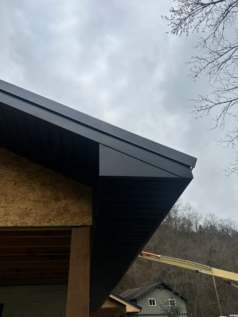 Crisp black metal fascia and rake trim running along the eave of a home under construction with exposed OSB sheathing