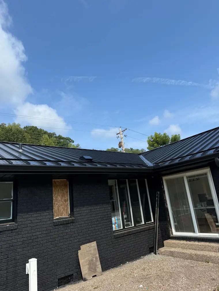 Single-story black-painted brick home with a new matte-black standing-seam metal roof and large picture windows