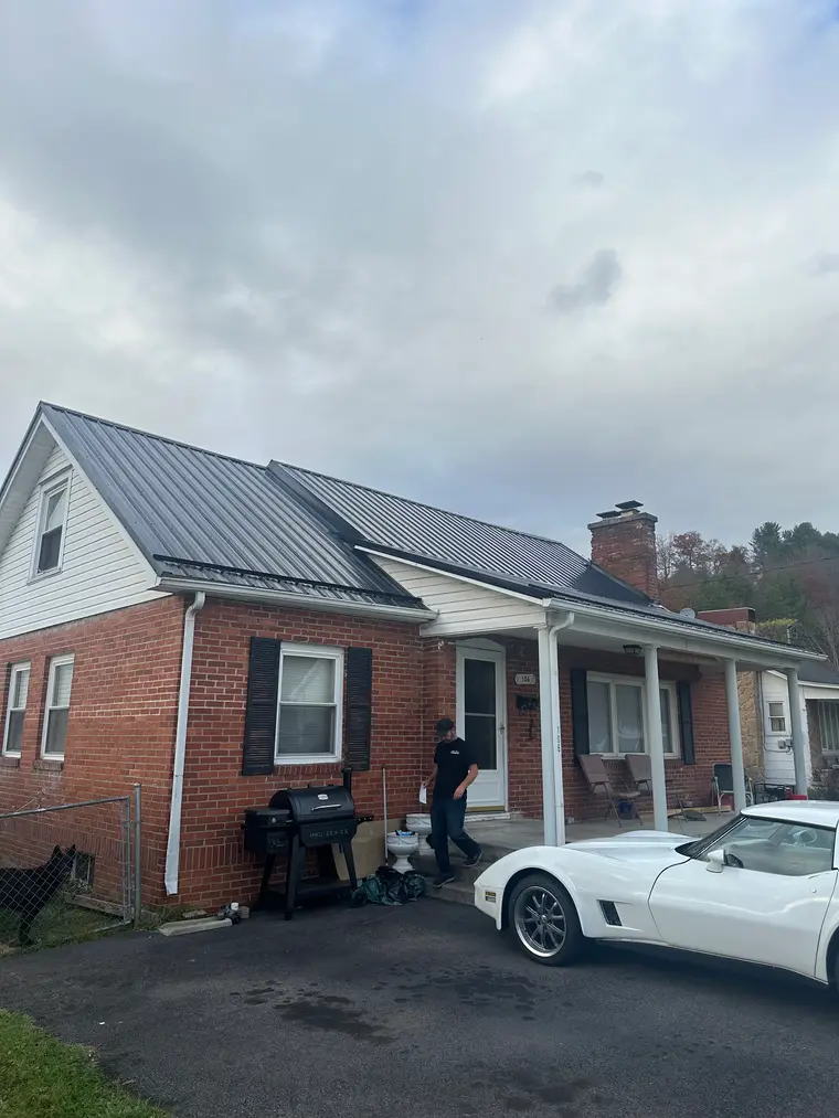 Red-brick Cape Cod home with a new black standing-seam metal roof and brick chimney, a white Corvette parked in the driveway