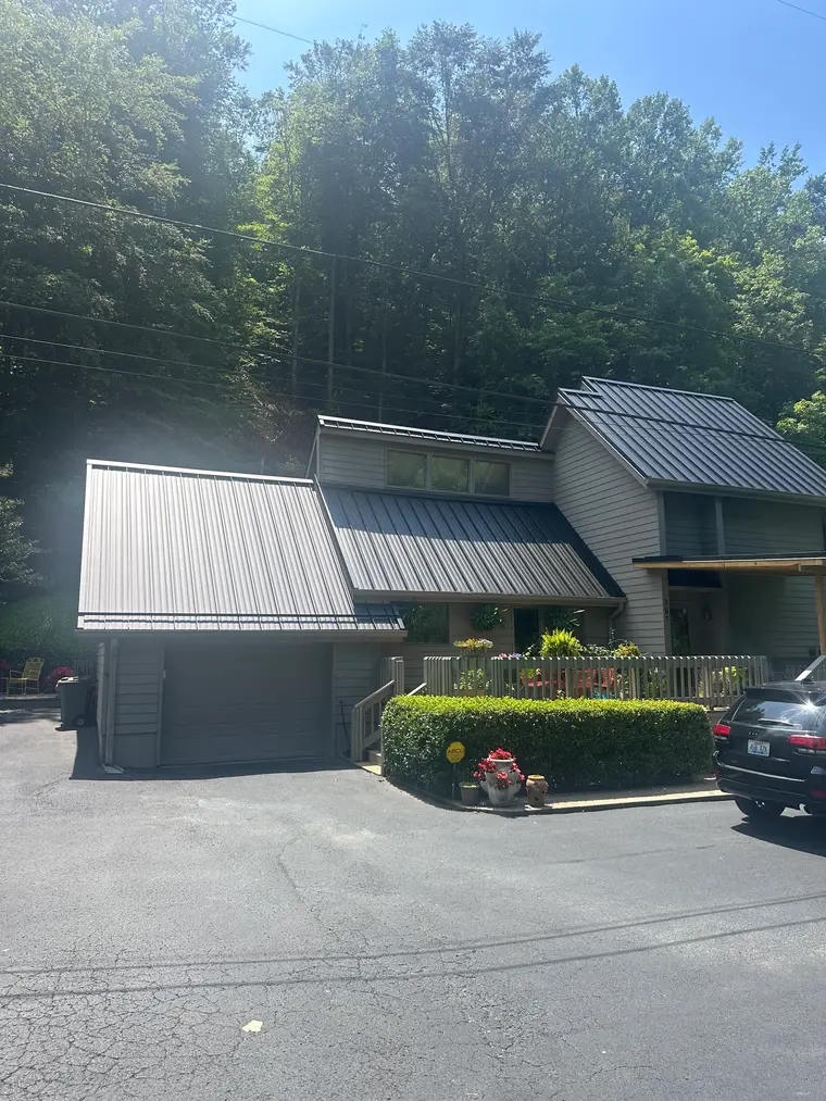 Contemporary two-story home set against a wooded hillside with a new charcoal standing-seam metal roof over the main house and attached garage