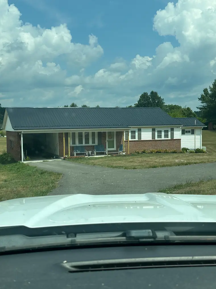White and brick country ranch home with a carport and a new black metal roof, photographed from the road
