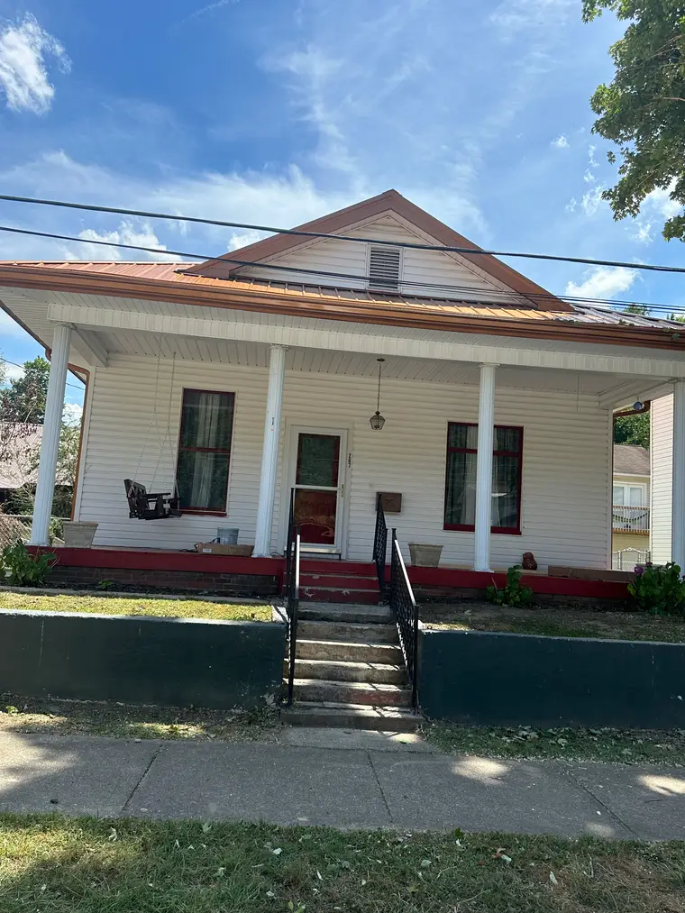 Front of the white historic farmhouse showing the columned porch and new clay-colored metal roof