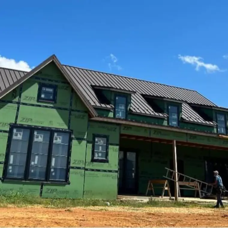 New-construction home sheathed in green panels with a black metal roof and matching dormers under a bright blue sky
