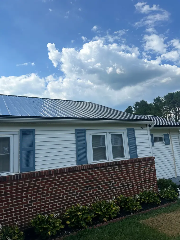 White vinyl-sided ranch home with a brick base, blue shutters, and a slate-blue standing-seam metal roof