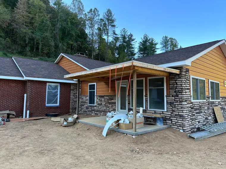 Rear of the cedar-tone sided home showing stacked-stone veneer and a covered patio under construction