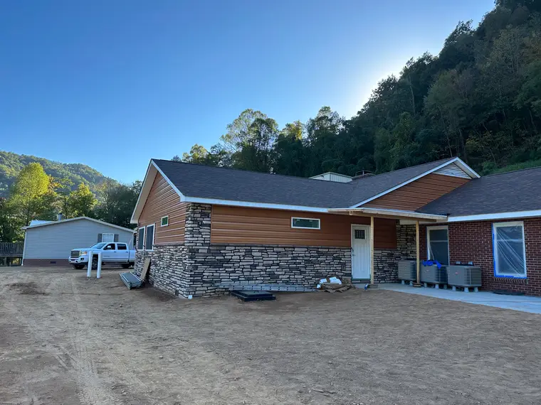 Cedar-tone sided home with stone veneer and brick in evening light, white pickup parked in the dirt yard