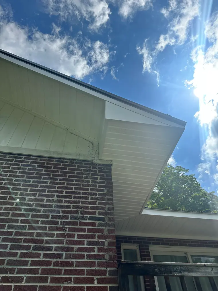 White vinyl soffit and fascia installed under a roof eave above red brick, bright sun in a blue sky